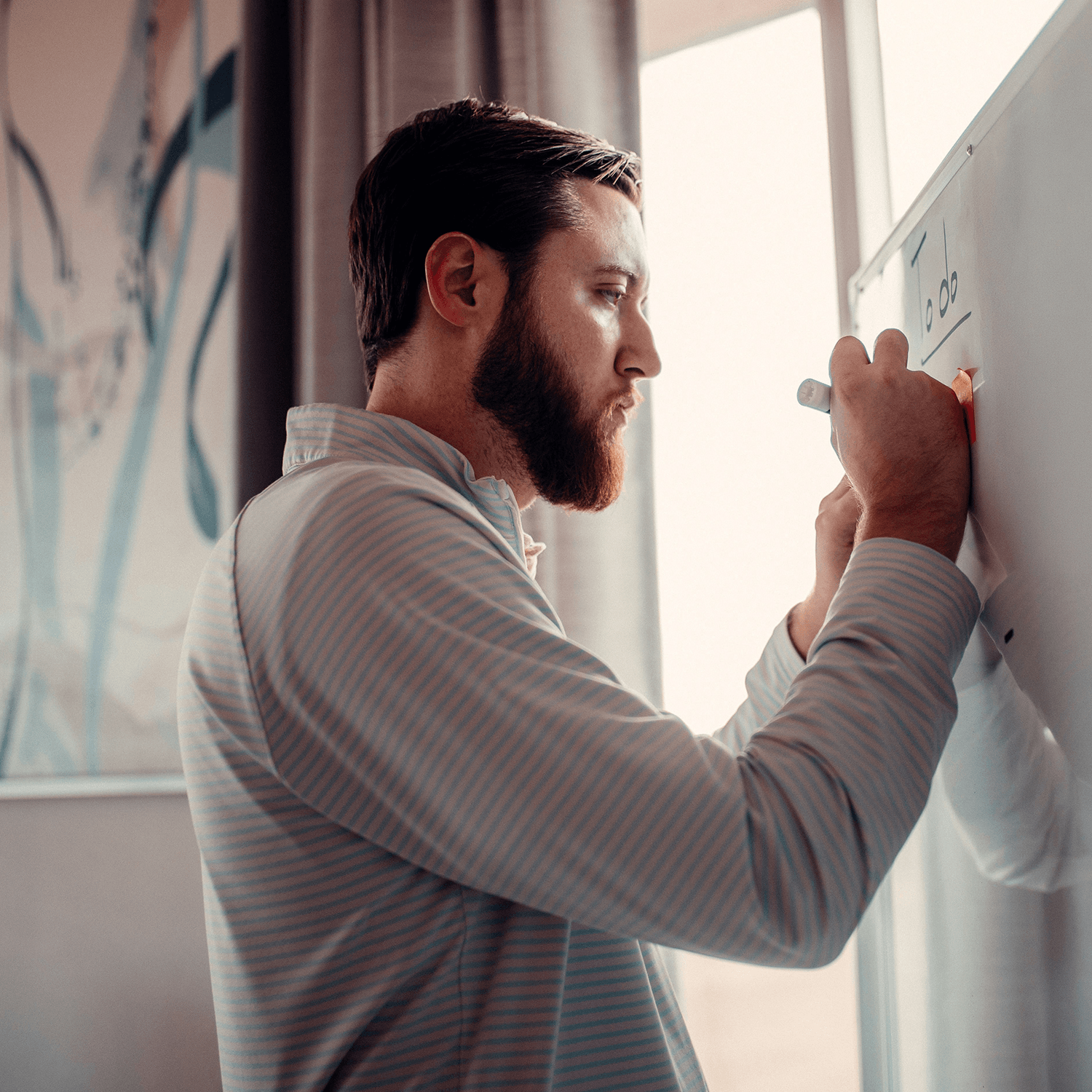 Ein junger Mann mit Vollbart schreibt etwas an einem Whiteboard